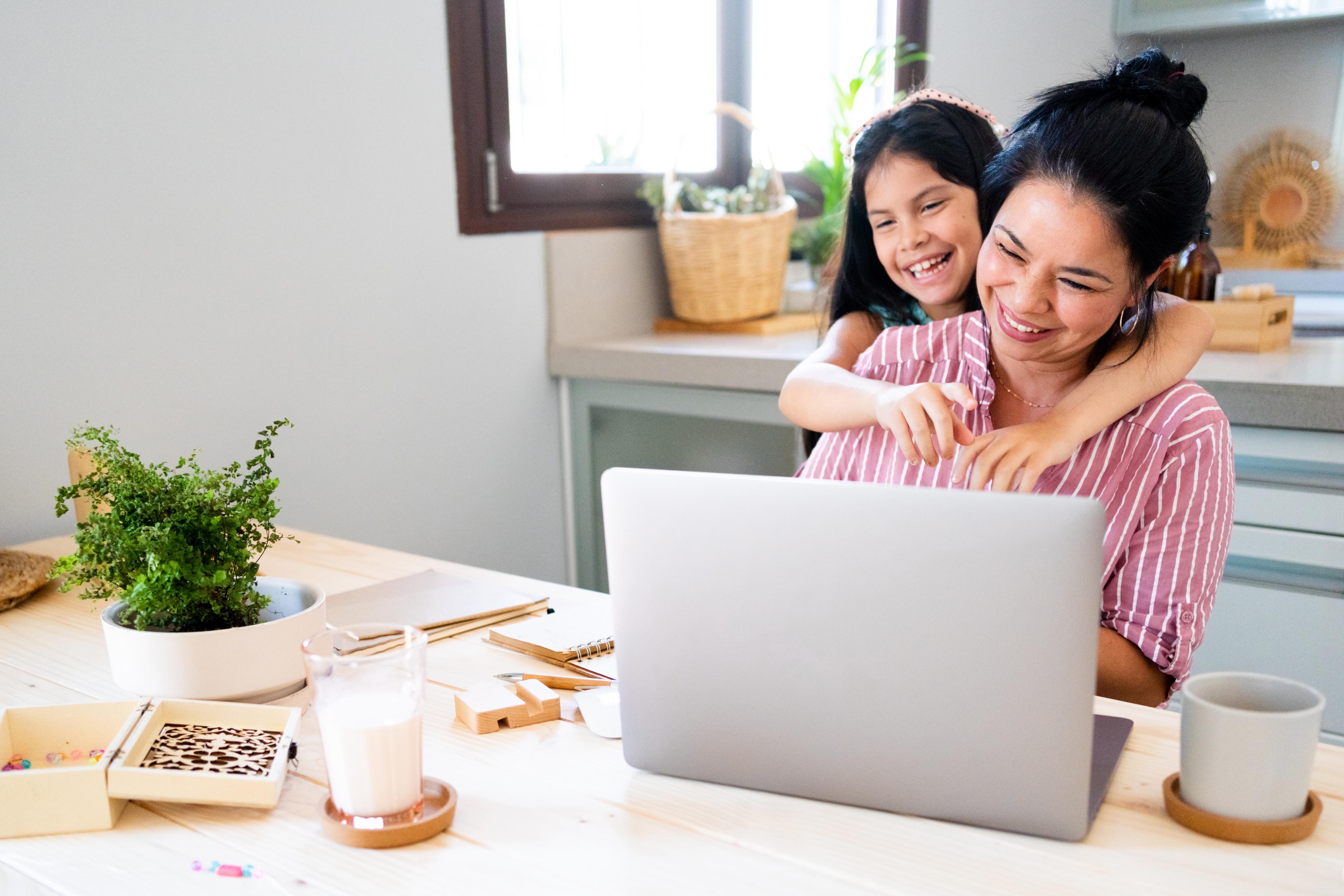 A mom and her daughter smile while looking at their laptop during a virtual call with their dietitian.